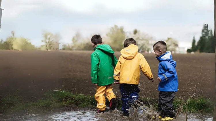 Trois enfants dans des imperméables colorés éclaboussant dans une flaque.